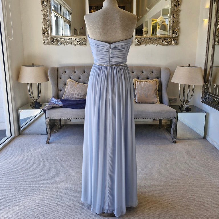 A floor-length light blue strapless gown displayed on a dress form mannequin in a furnished room with a sofa, lamps, and mirrors.