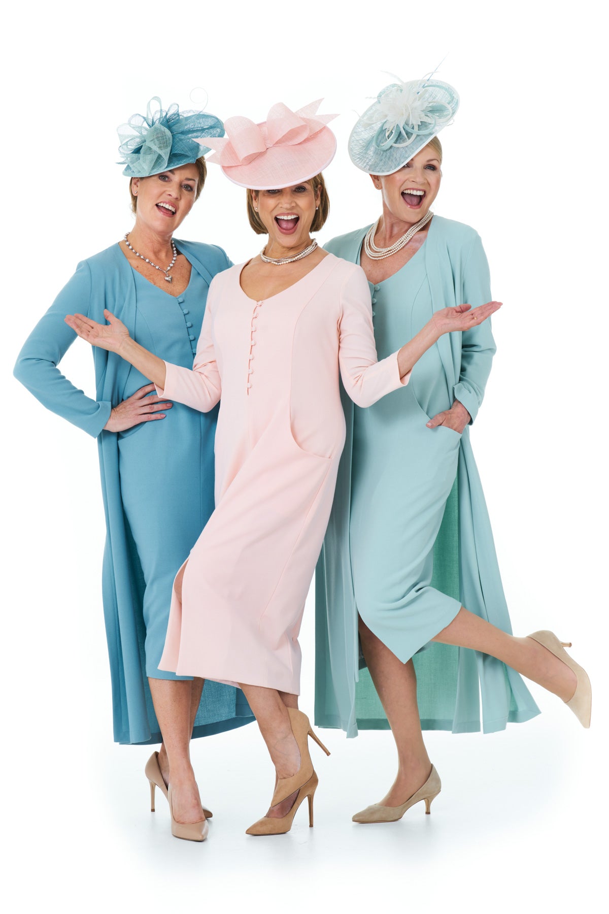 Three women modeling elegant 1920s-style dresses and fascinator hats in pastel blue, pink, and mint green on a white studio background.